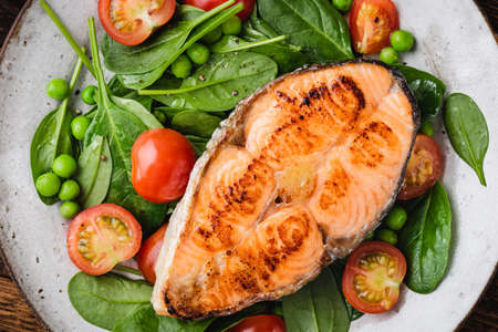 Roasted salmon steak served with greens and cherry tomatoes. Healthy dinner or lunch mealの写真素材