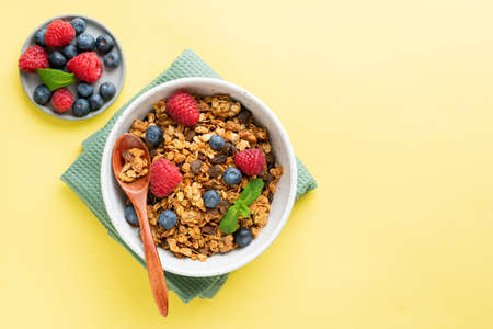 Granola in bowl with fresh berries on yellow background, top view. Healthy breakfast cerealsの写真素材