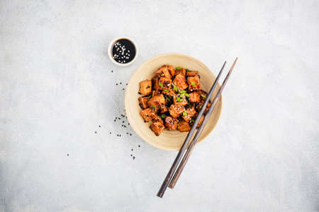 Fried marinated tofu with sesame seeds on grey concrete background, top view. Healthy vegan meat...