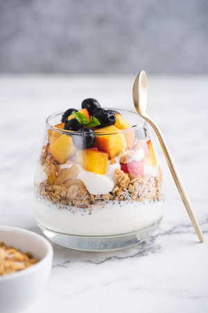 Greek yogurt with granola and fruits in jar on white marbleの写真素材
