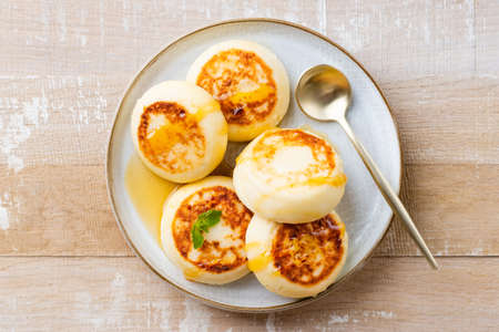 Syrniki, cottage cheese fritters with honey on plate, isolated on wooden table background top view
