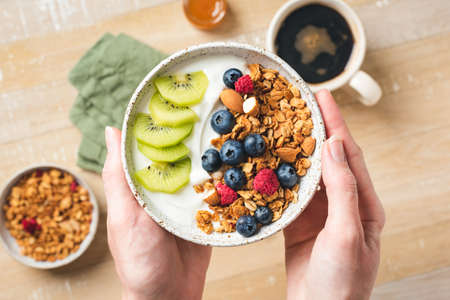 Yogurt and granola bowl with berries in female handsの写真素材
