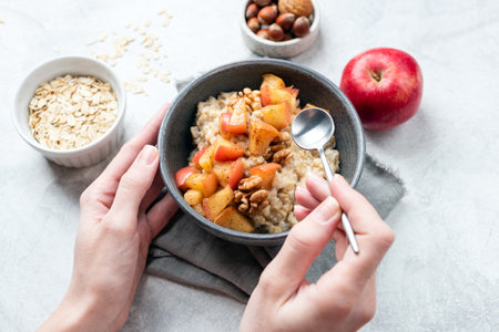 Oatmeal bowl with apple and cinnamon in woman's hands. Concept of vegan diet, clean eating, guilt...