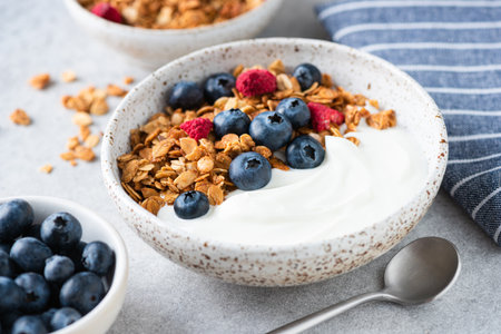 Bowl of yogurt with granola, dry raspberries and blueberries. Healthy breakfast meal, concept of...