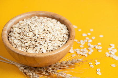 Rolled oats, oat flakes in wooden bowl on yellow background. Summer agriculture food harvest conceptの写真素材