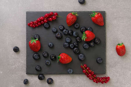 fresh strawberry blueberry and red currant on a black slate on gray stone background. top view.の写真素材