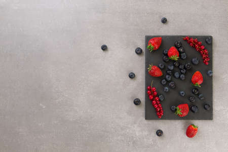 fresh strawberry blueberry and red currant on a black slate on gray stone background. top view. copy space.の写真素材