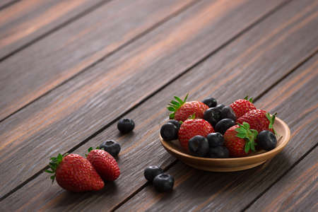 strawberry and blueberry in a wooden plate on wooden background. copy space.の写真素材