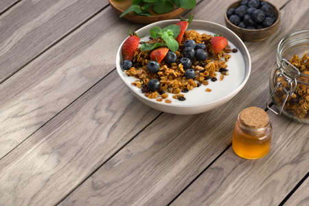 Bowl of homemade granola with yogurt and fresh berries on wooden background. copy space.