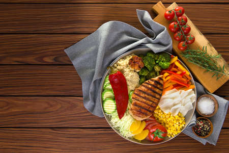 Healthy salad dish with grilled chicken, quinoa, garlic cabbage pepper bell, bell pepper orange, tomato, corn, barbecue. healthy eating. wooden background top view. copy space.の写真素材