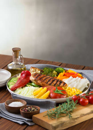 Healthy salad dish with grilled chicken, quinoa, garlic cabbage pepper bell, bell pepper orange, tomato, corn, barbecue. healthy eating. wooden/stone background. copy space.の写真素材