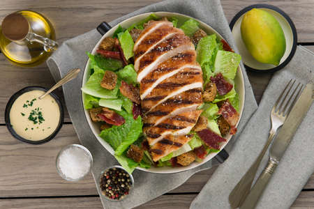 Classic Caesar Salad bowl and dressing. wooden background. top view.の写真素材