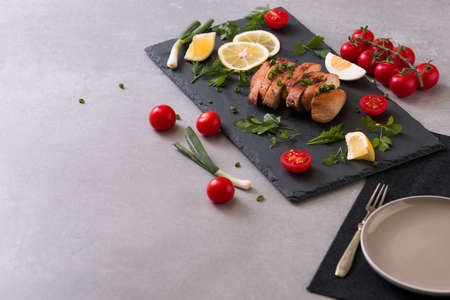 roasted/baked chicken breast on a slate plate with herbs and cherry tomatoes, lemon and egg . Healthy eating scene. stone backgroundの写真素材