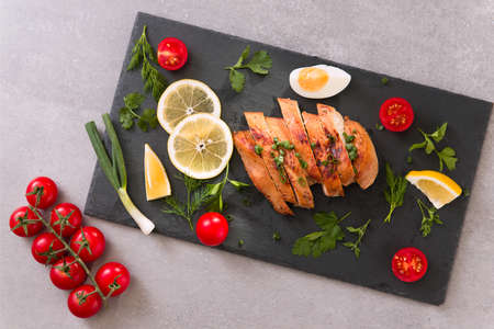 roasted/baked chicken breast on a slate plate with herbs and cherry tomatoes, lemon and egg . Healthy eating scene. stone background. top viewの写真素材