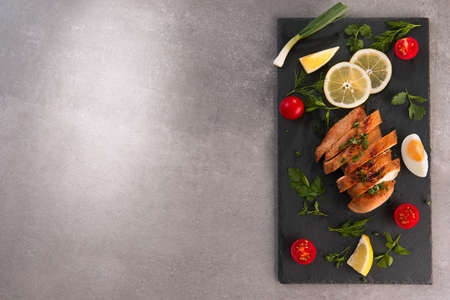 roastedbaked chicken breast on a slate plate with herbs and cherry tomatoes, lemon and egg . Healthy eating scene. stone background. top view. copy space.の写真素材