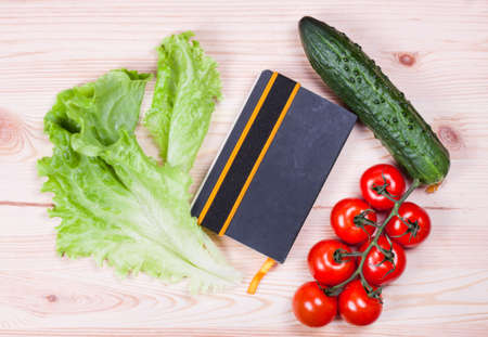 Notebook with recipes and vegetables on a wooden boardの写真素材