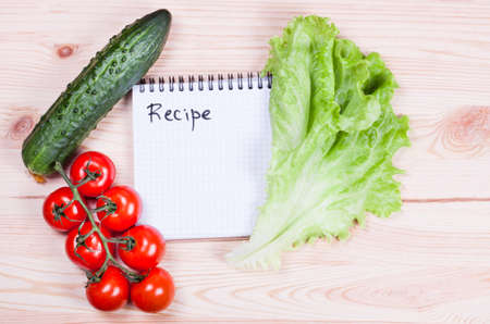 Notebook with recipes and vegetables on a wooden boardの写真素材