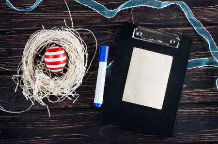 Easter eggs in the nest with clipboard on rustic wooden background