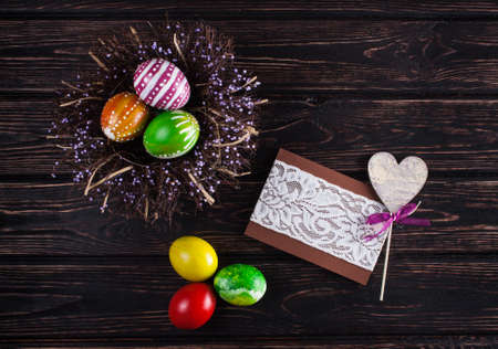 Easter eggs in the nest with card on rustic wooden background