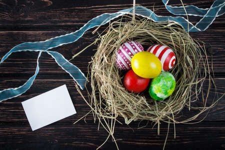 Easter eggs in the nest with card on rustic wooden background