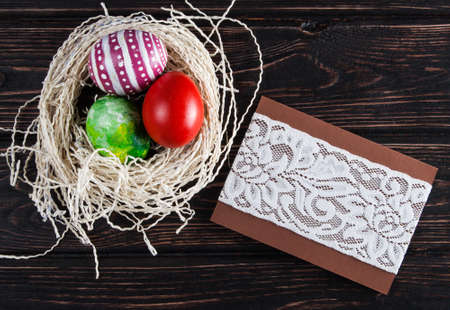 Easter eggs in the nest with card on rustic wooden background