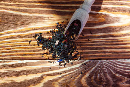 Black leaf tea with additives and a wooden spoon on the boardの写真素材