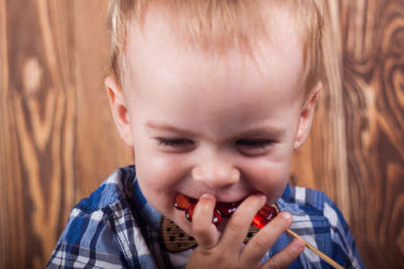 small child in a plaid shirt eating red  candyのeditorial素材