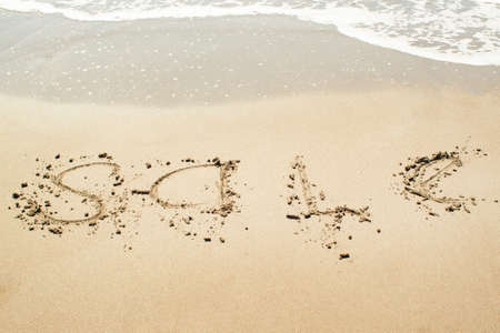 Sale sign on the beach, text written on the sandの写真素材