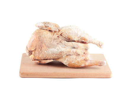 Frozen chicken carcass on a wooden chopping board isolated on white backgroundの写真素材