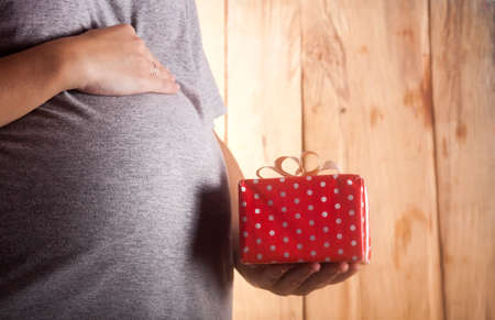 Image of pregnant woman touching her belly with hands and gift boxの写真素材