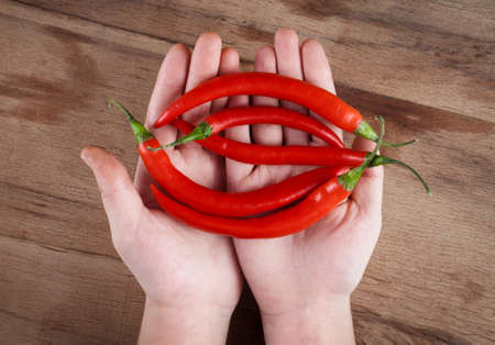 Red fresh chili in hand on wood desk. Food backgroundの写真素材