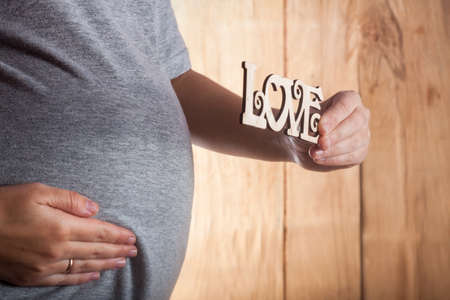 Image of pregnant woman touching her belly with hands on wood backgroundの写真素材