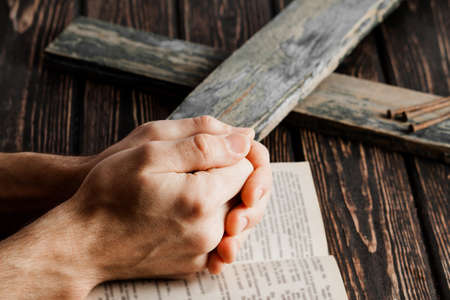 Crown of thorns with hands folded in prayer on wood desk. Christian concept
