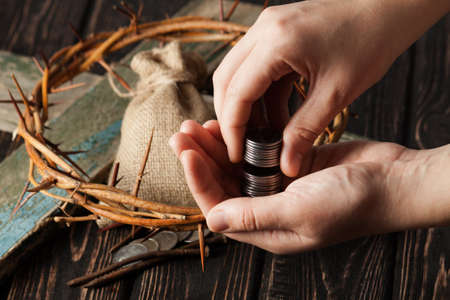 Crown of thorns with hands and coins on wood desk. Christian conceptの写真素材