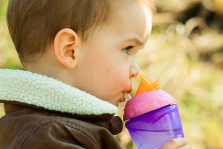 Child drinks water from a baby bottle in natureの写真素材