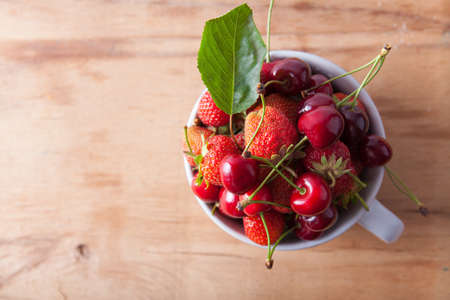 Cherry and strawberry in bowl close up on wood deskの写真素材