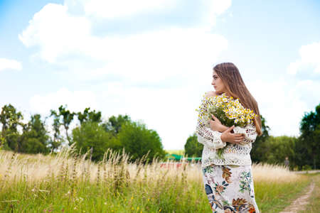Fashion beautiful girl in the field with bouquet of wildflowersの写真素材