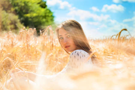 Fashion beautiful girl in the field with yellow spikelets on the sky backgroundの写真素材