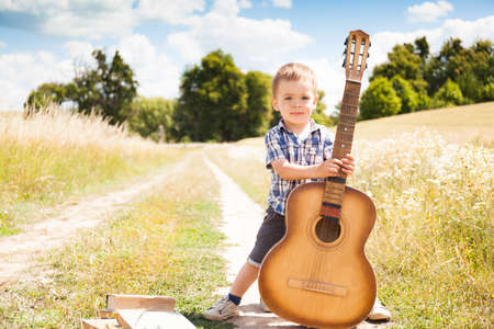Fashion little boy with guitar outside in natureの写真素材