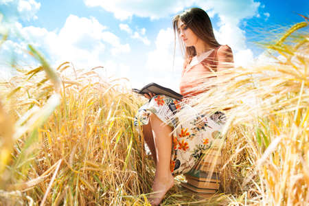 Fashion beautiful girl in the field with yellow spikelets on the sky background with book