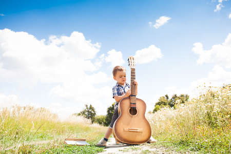 Fashion little boy with guitar outside in natureの写真素材