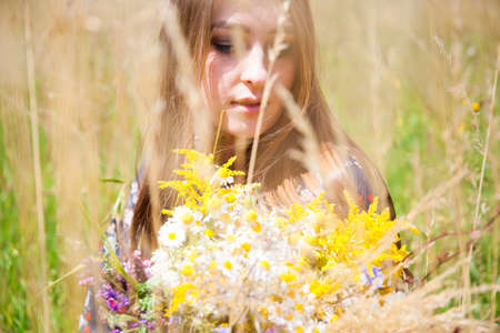 Fashion beautiful girl in the field with bouquet of wildflowersの写真素材