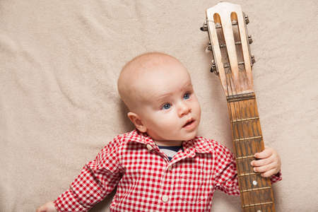 Small child boy with guitar on bed