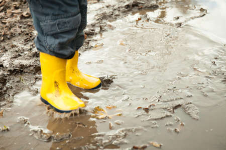 child in yellow rubber boots plays in a puddle