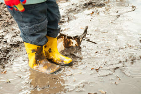 child in yellow rubber boots plays in a puddleの写真素材