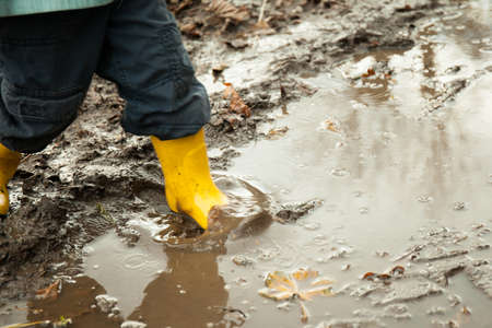 child in yellow rubber boots plays in a puddleの写真素材