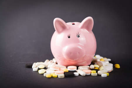 Pills close up on black background and money box pig. Medical conceptの写真素材