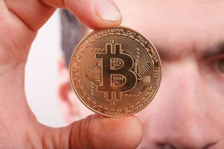 crazy bitcoin lover with golden coin by eyes; funny miner with btc near faceの写真素材