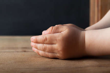 Hands of praying young man on a wooden desk background.の写真素材