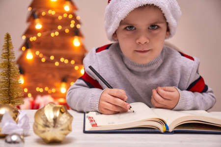 Christmas Child Write Letter to Santa Claus, Kid in Santa Hat Writing Wish List, unfocused lights backgroundの写真素材